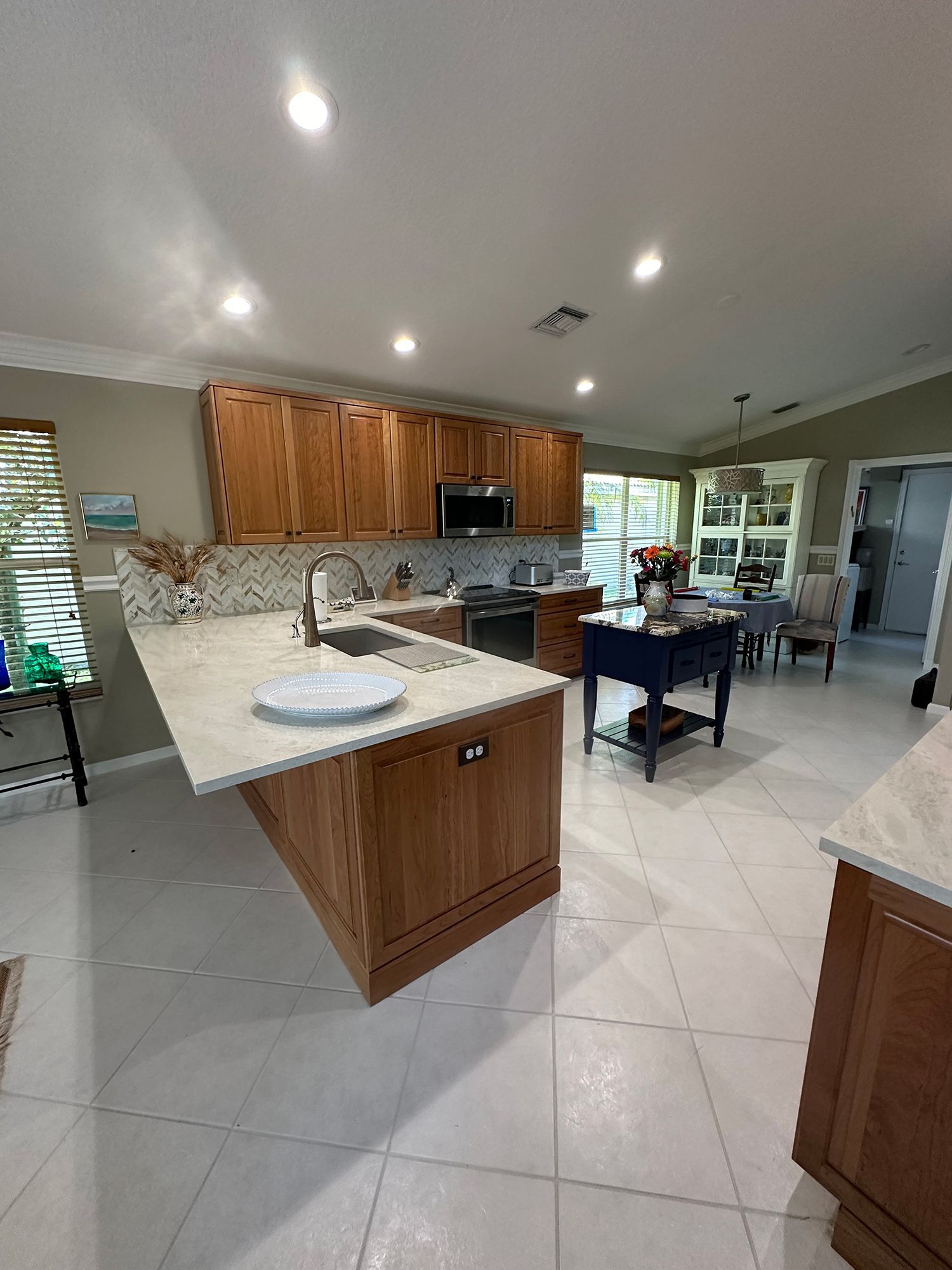 Kitchen with wooden cabinets, white countertops, and white tile flooring. Dining area visible.
