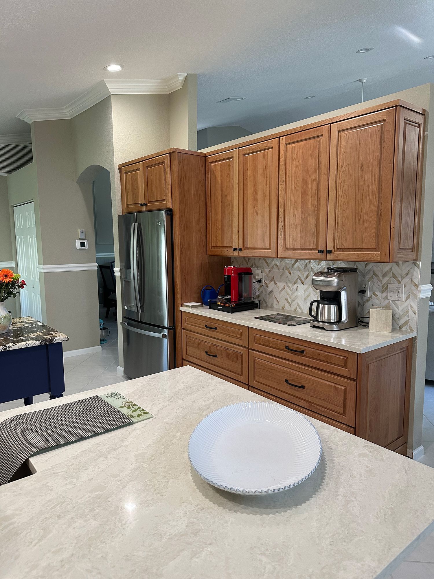 Kitchen with light wood cabinets, stainless steel refrigerator, white countertops, and coffee maker.
