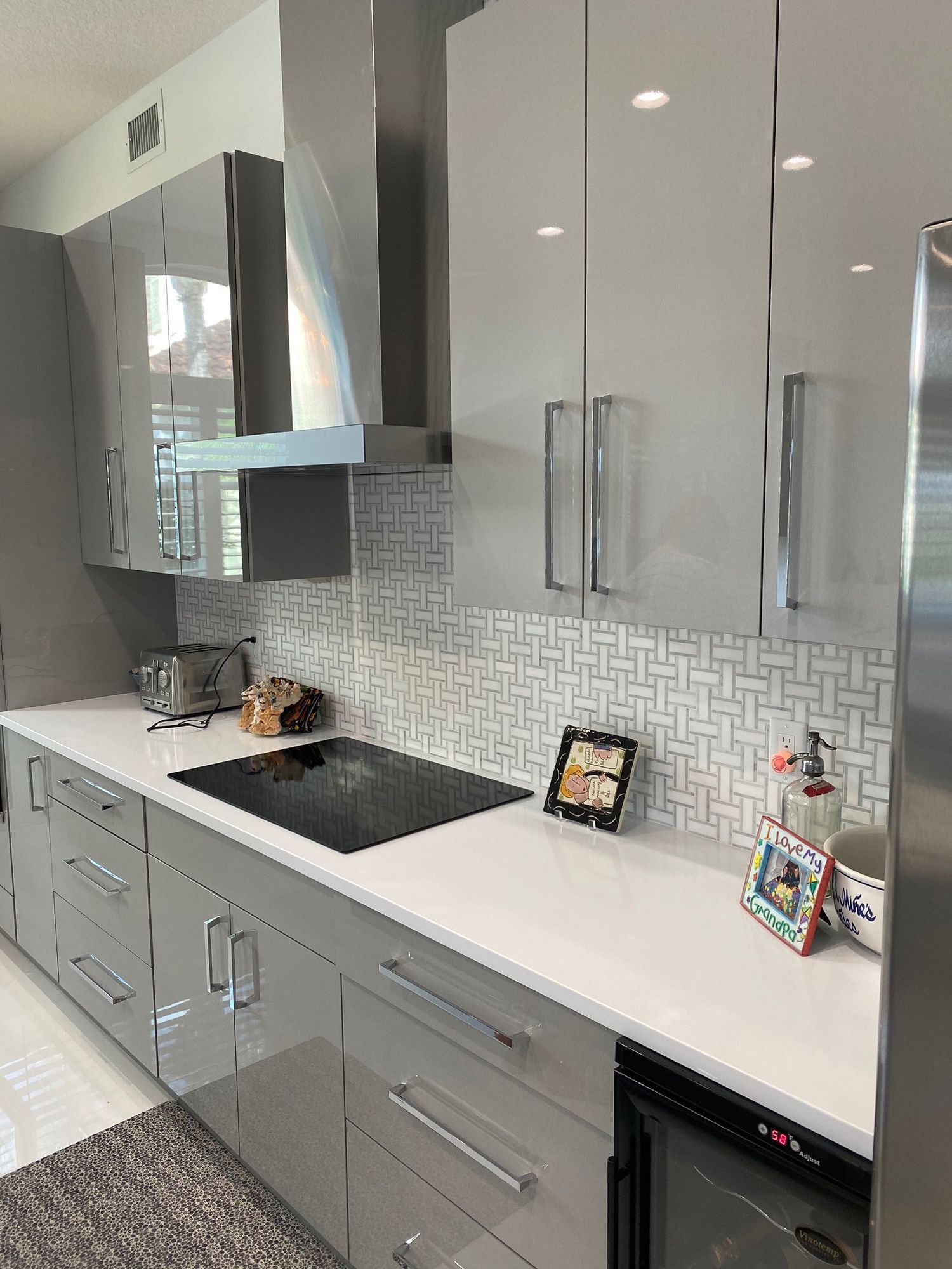 Modern kitchen with gray and white cabinets, stainless steel range hood, white countertops, and mosaic backsplash.