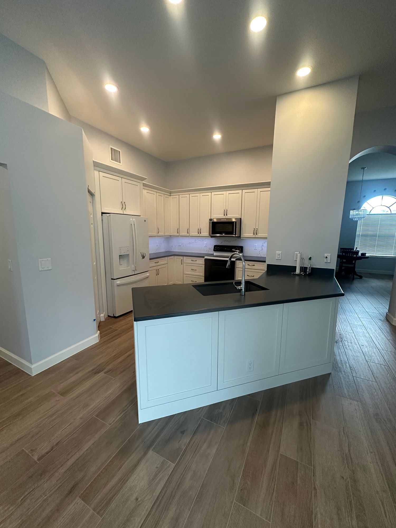 Modern kitchen with white cabinets, dark countertops, and wood-look flooring.