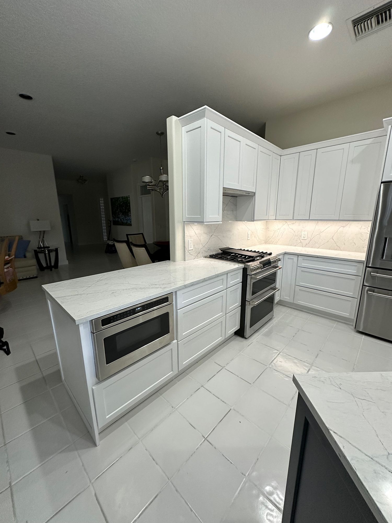 White kitchen with island, cabinets, appliances, and white tile floor.