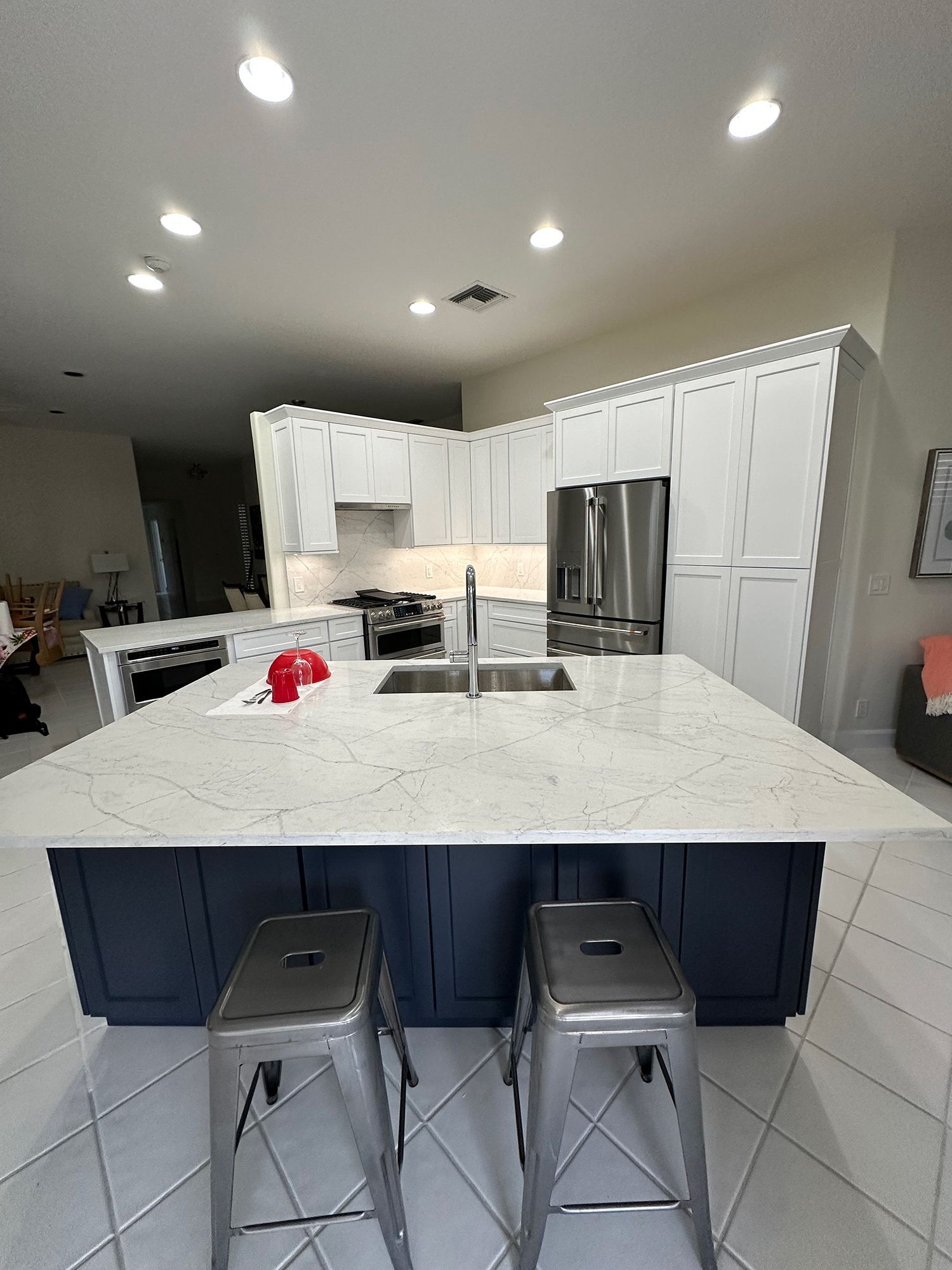 Kitchen with blue island, white countertops, stainless steel appliances, and metal stools.