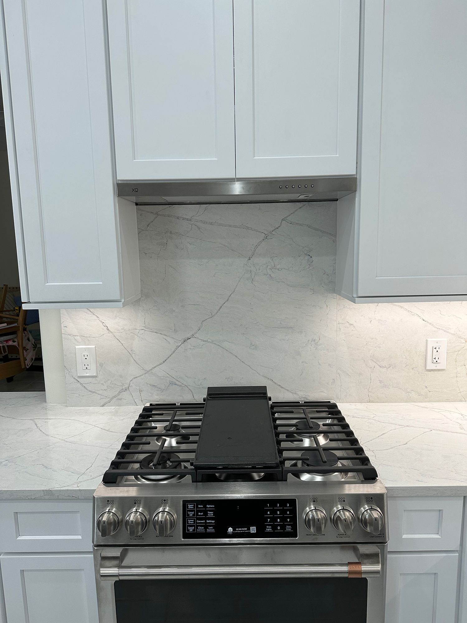 Kitchen with white cabinets, gas range, marble backsplash, stainless steel hood, and countertop.