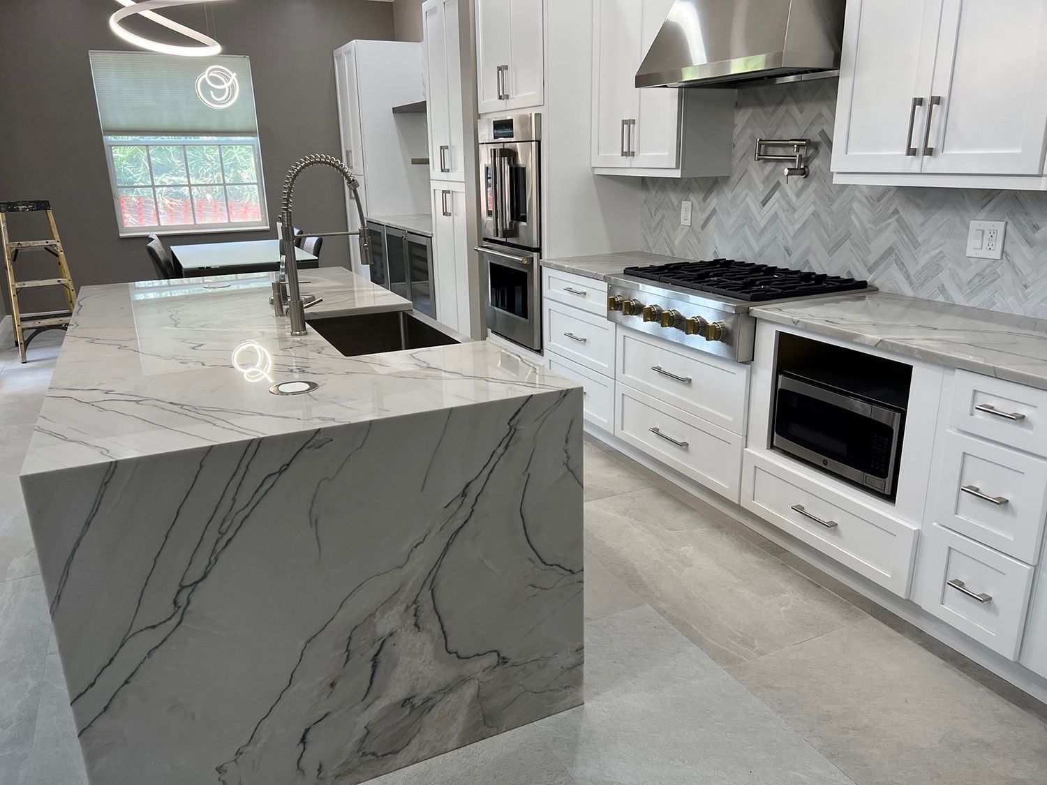 Modern kitchen with white cabinets, marble island and countertops, stainless steel appliances.