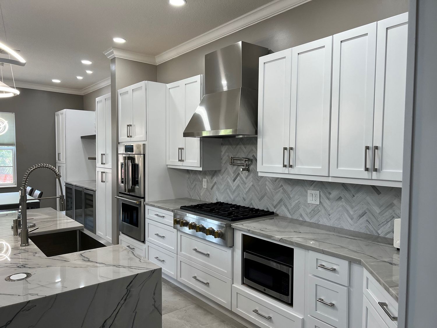Modern white kitchen with stainless steel appliances, marble countertops, and gray walls.