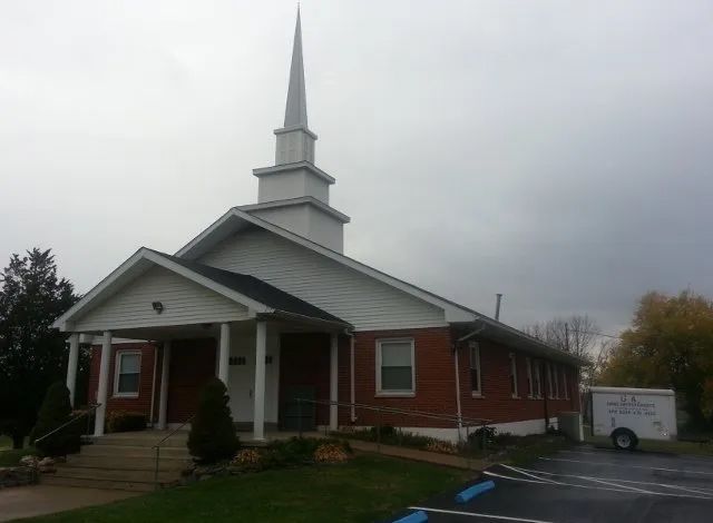 A church with a steeple and a parking lot in front of it
