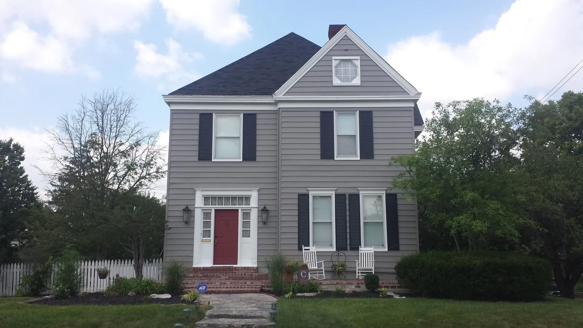 A grey house with black shutters and a red door