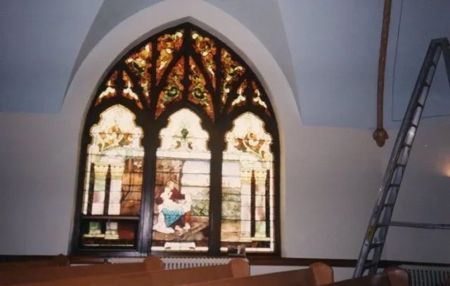 A stained glass window in a church with a ladder in the background