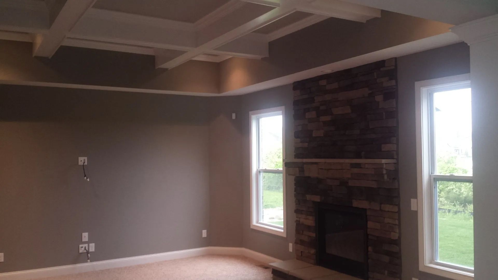 An empty living room with a fireplace and two windows.