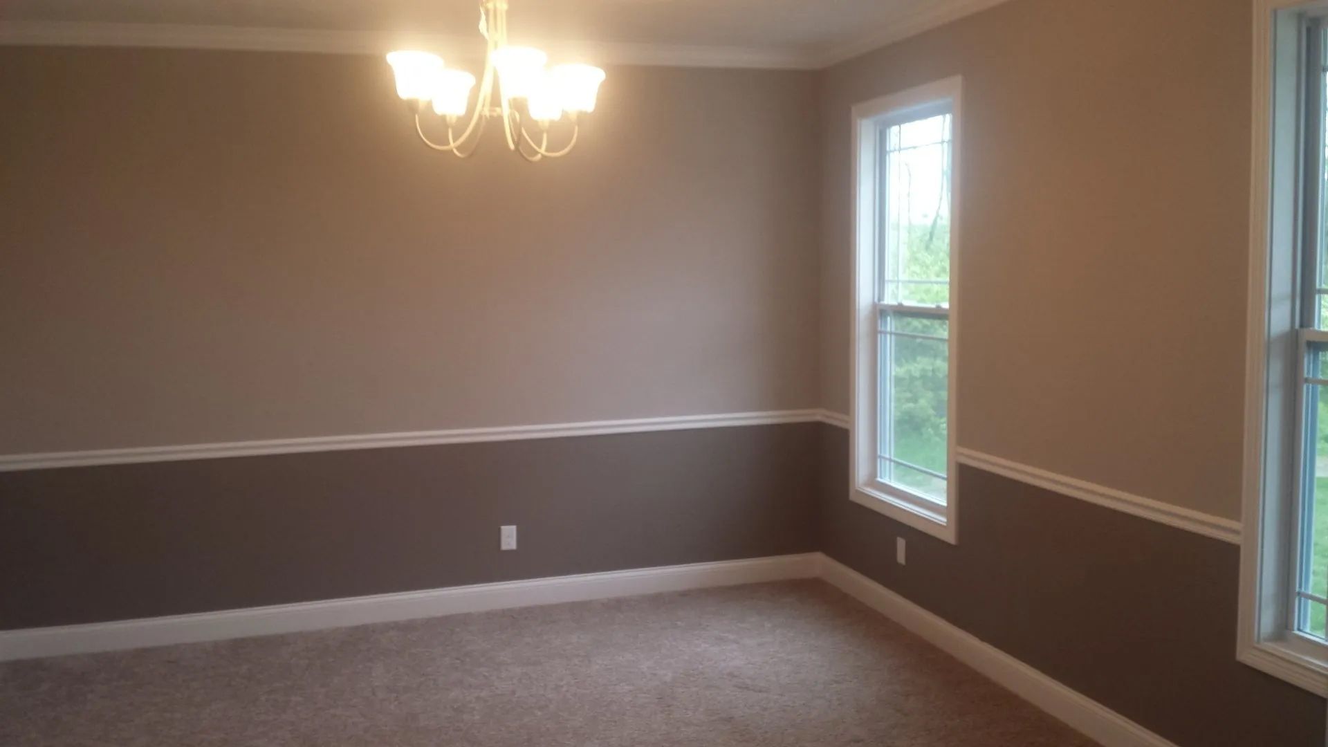 An empty room with a chandelier and two windows.