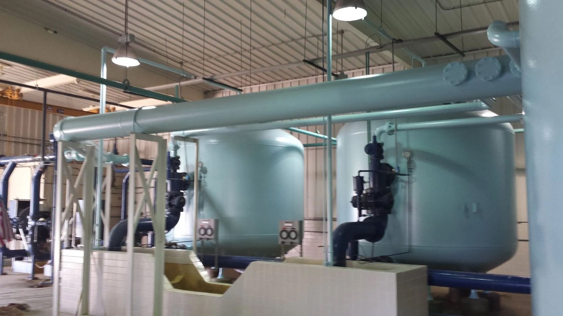 A man is sitting on top of a large tank in a factory.