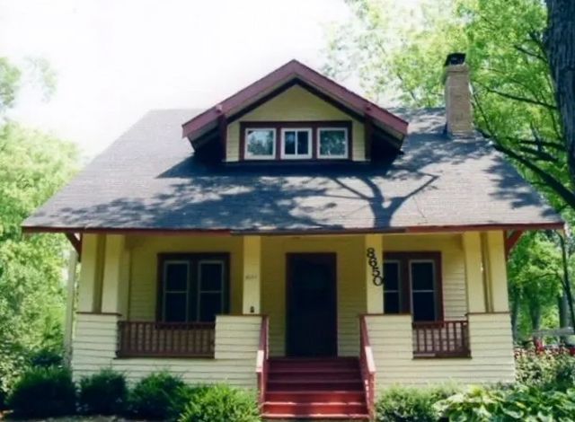 A house with a porch and a chimney is surrounded by trees