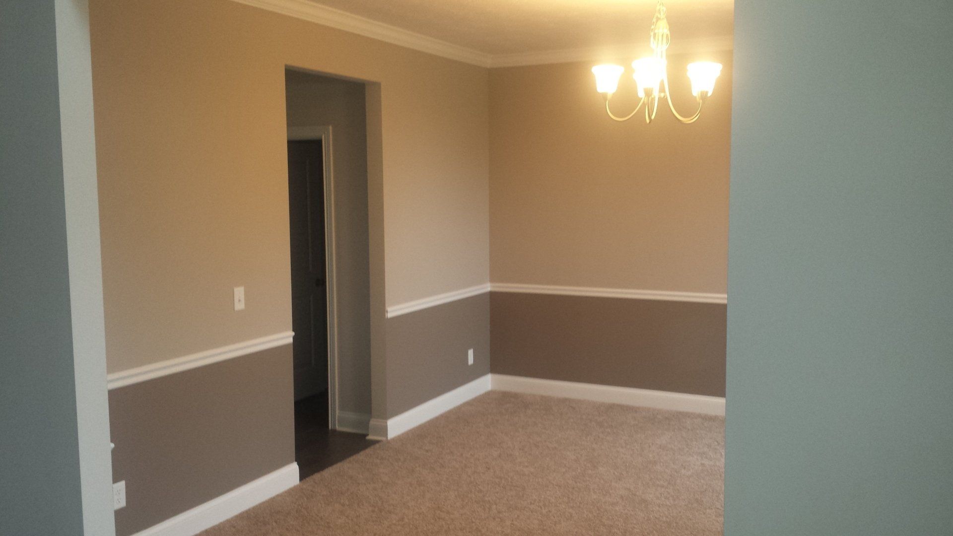 An empty dining room with a chandelier hanging from the ceiling.