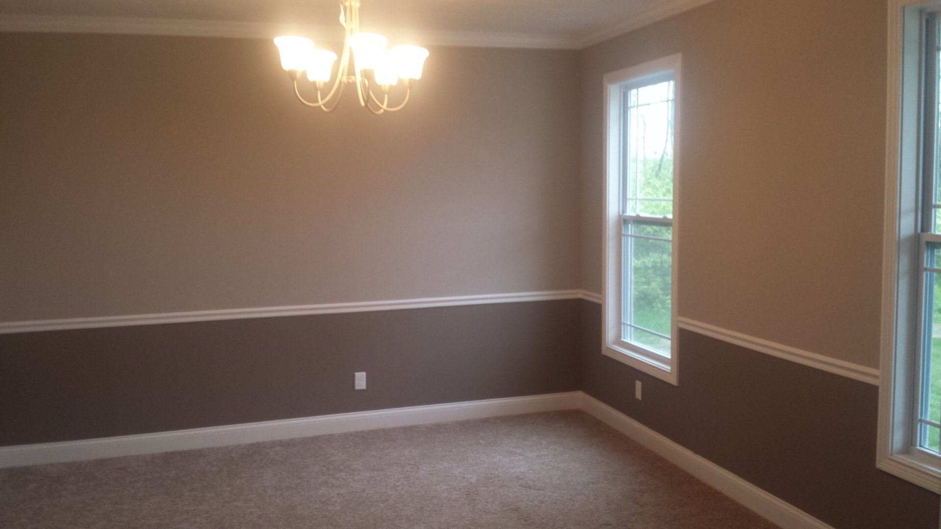 An empty room with a chandelier and two windows.