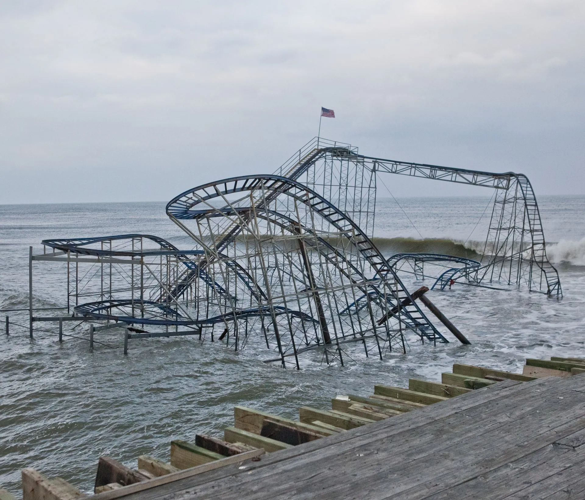 Collapsed rollercoaster in ocean water with an American flag atop.