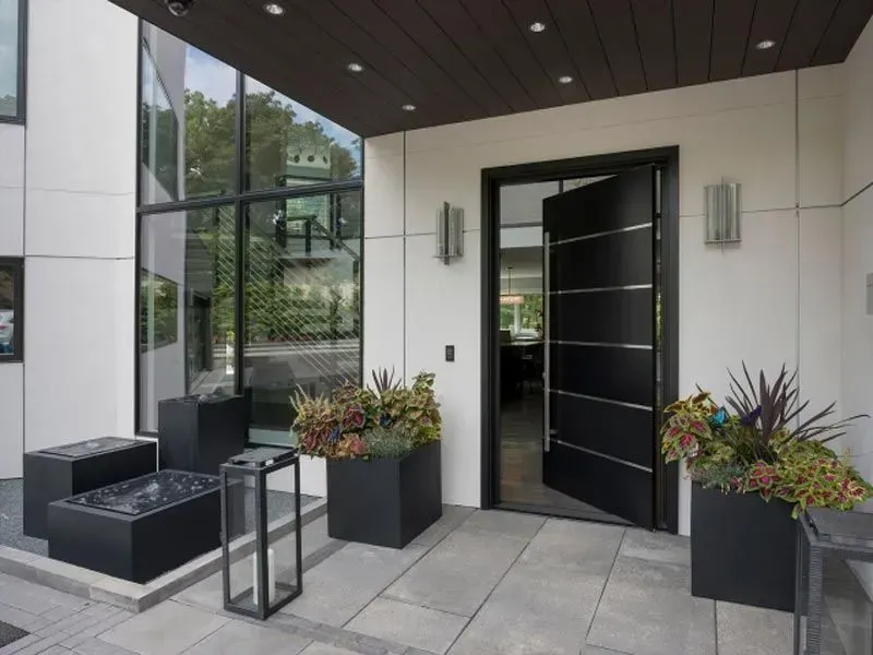 Modern home entrance with black door, planters, and large windows.
