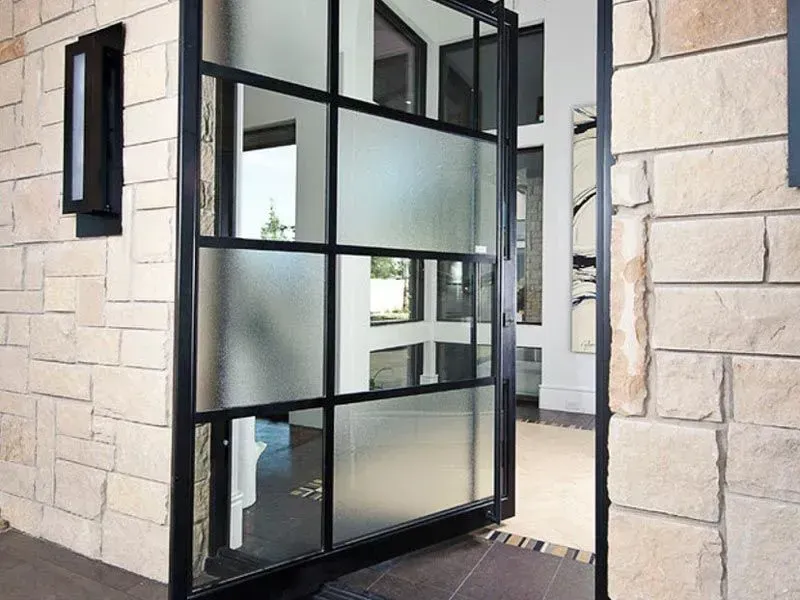 Black-framed glass door, open, set in a stone wall. A modern entry with frosted glass panes.