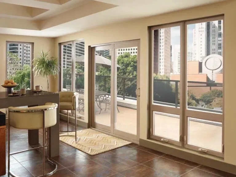 Interior view of a room with large windows overlooking a city and patio. Beige walls, brown floor, and a bar with stools.