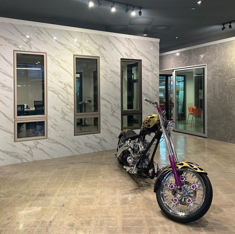 Chopper motorcycle parked inside a showroom with marble-look wall panels and windows.