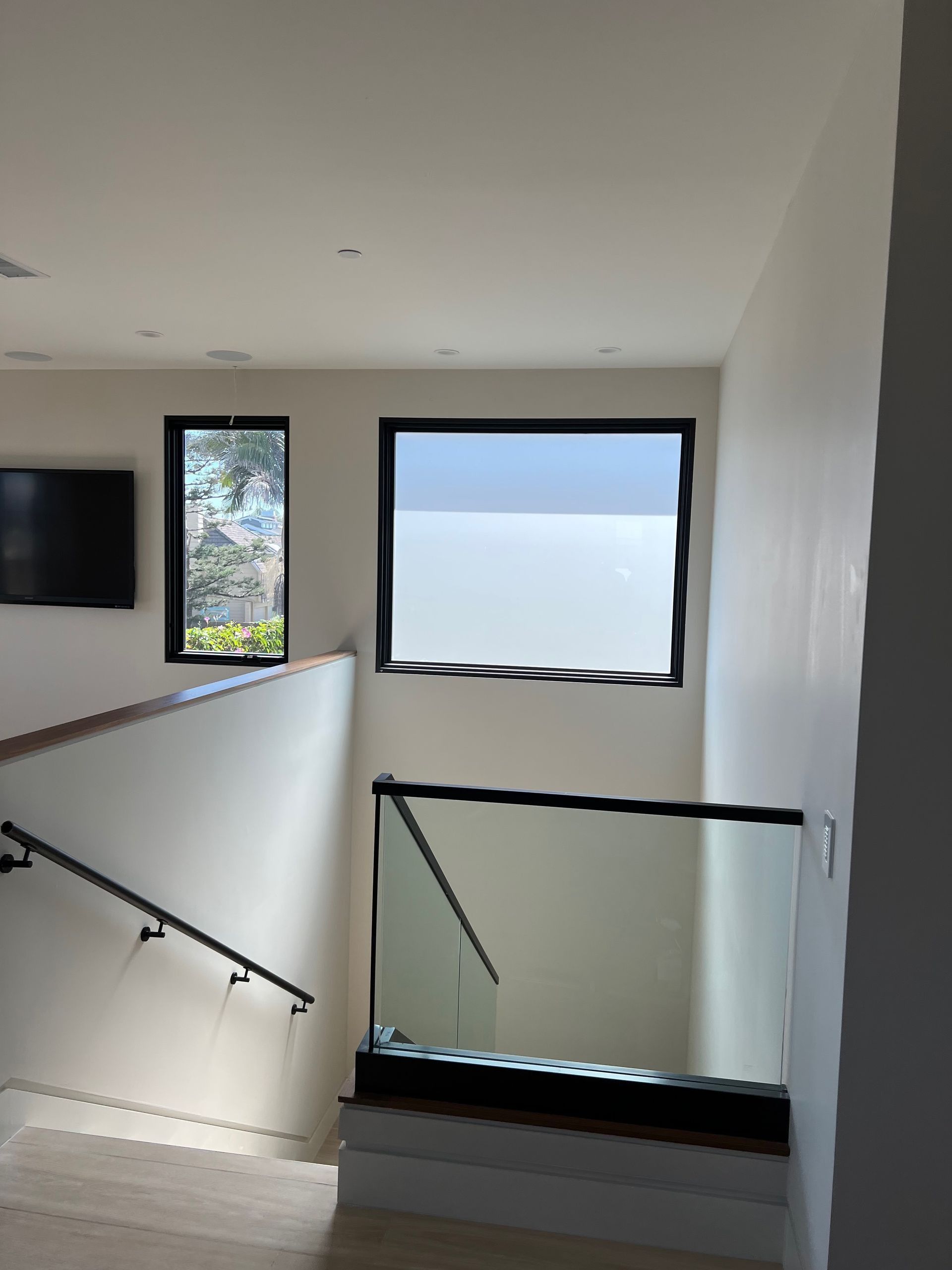 Staircase with glass railing, two windows with black frames, and white walls.
