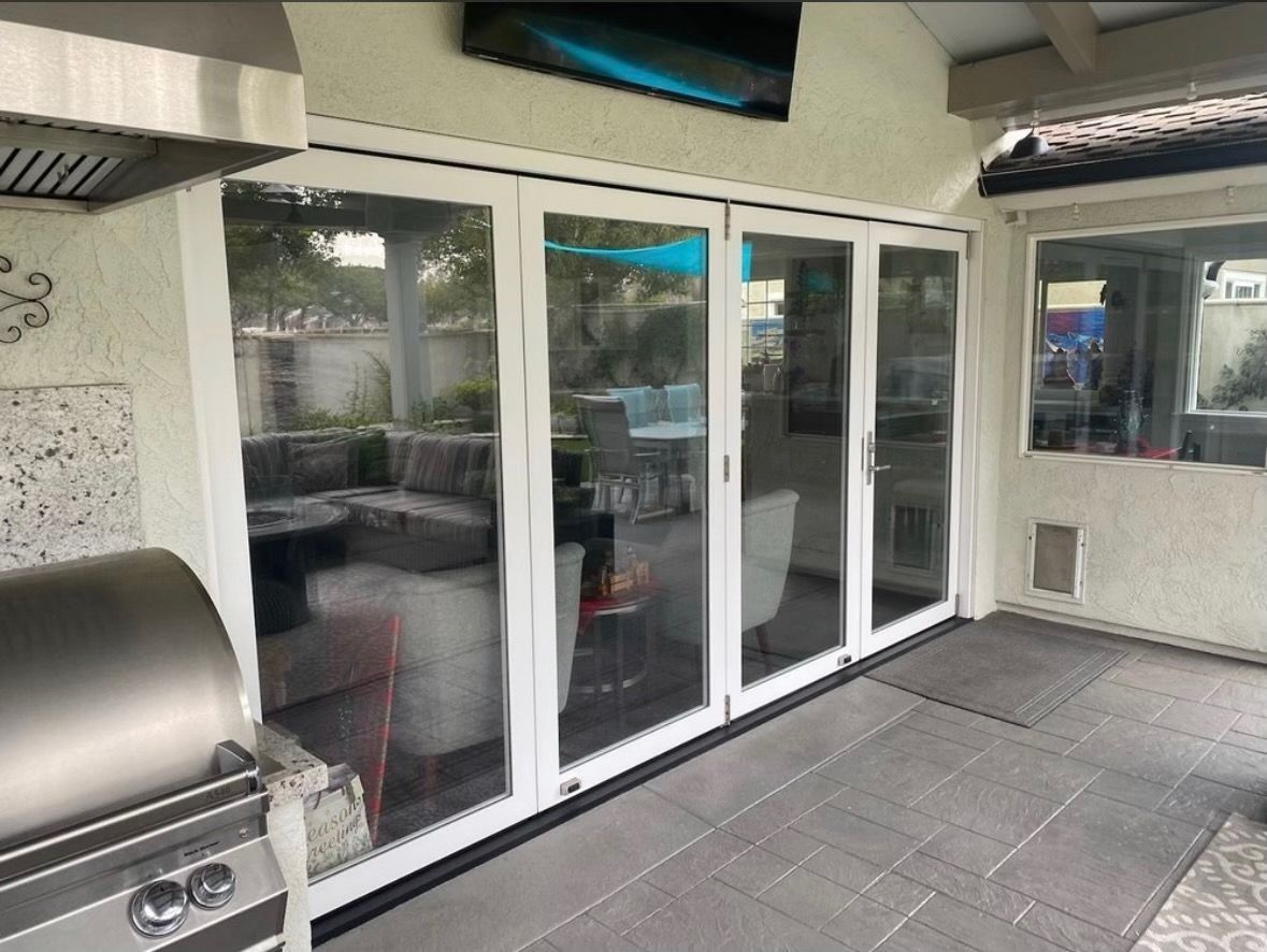 Patio with bi-fold glass doors, gray tiled floor, outdoor grill, and a television.