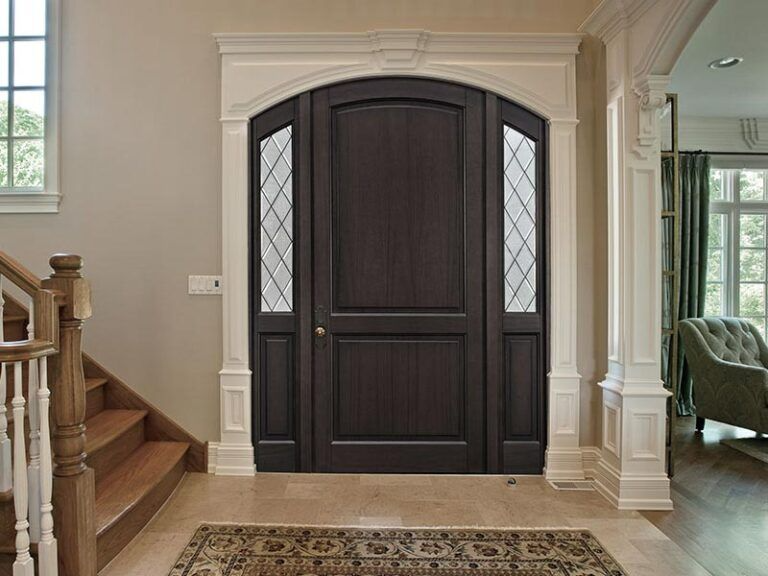 Dark wooden front door with sidelights, cream trim, and a small rug on a tiled floor.