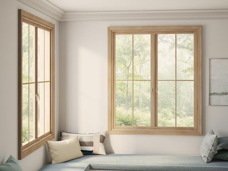 Corner window seat with two wood-framed windows overlooking a green landscape. Pillows on the seat.