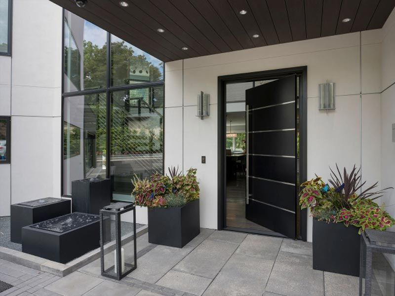 Modern house entrance with open black door, large windows, planters, and stone patio.