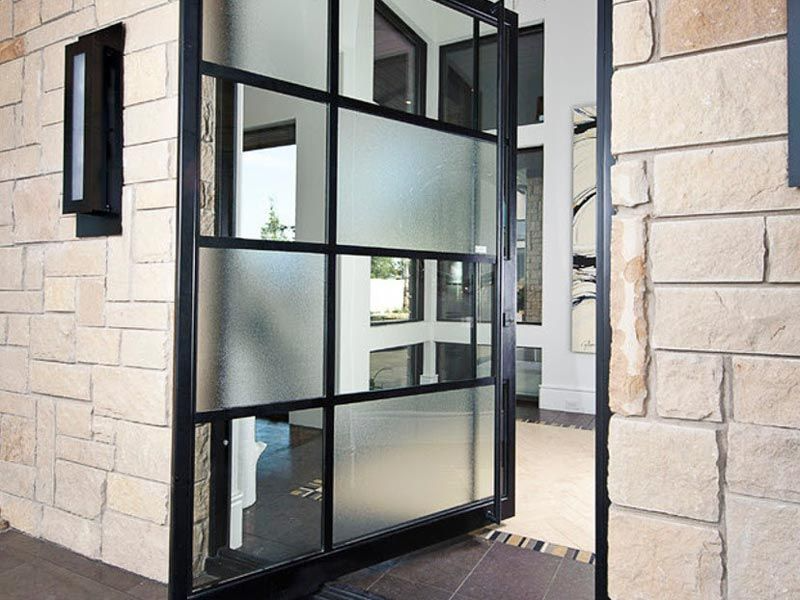 Black-framed glass door, open, set in a stone wall. A modern exterior with natural light.