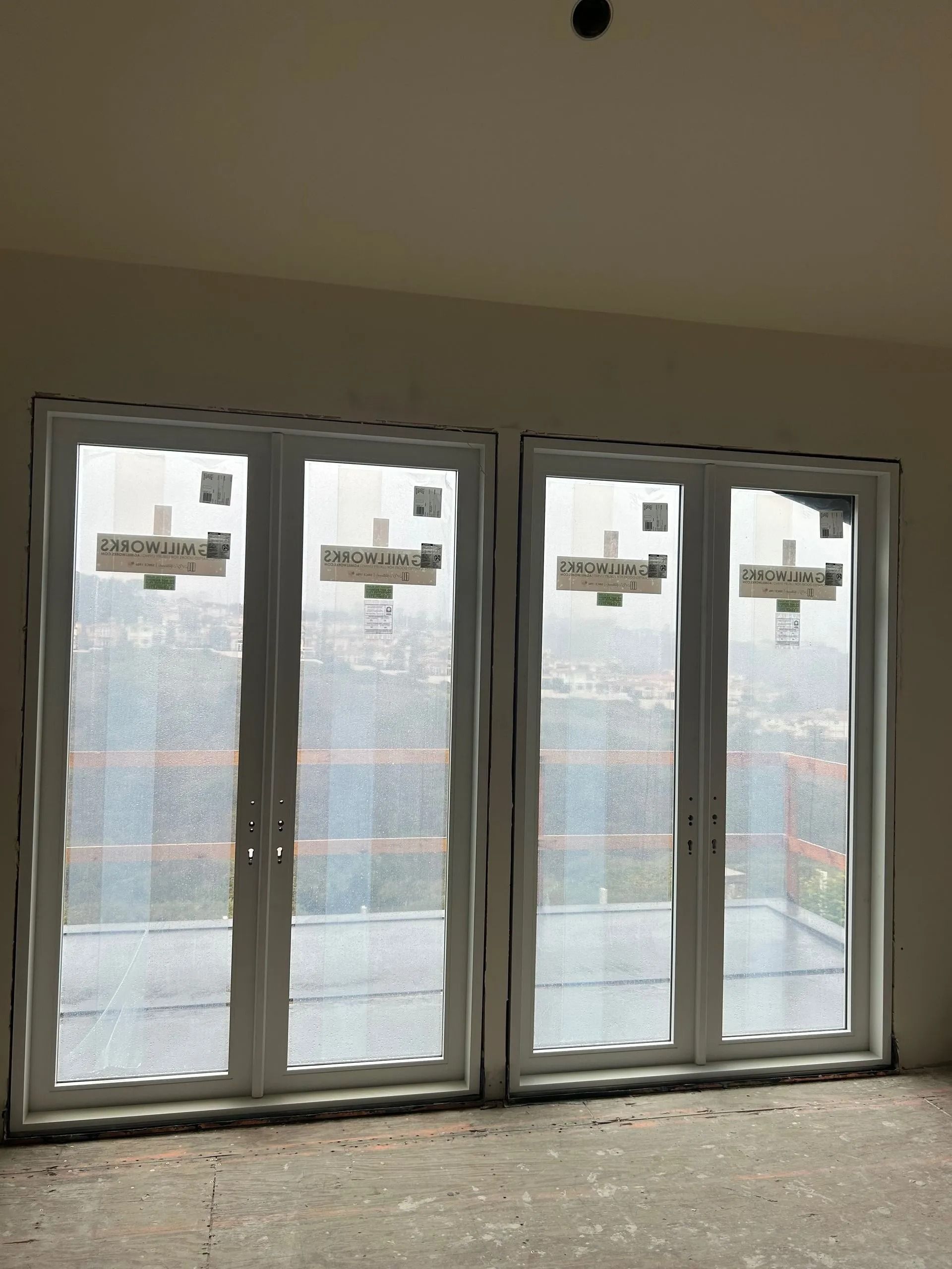 Two white framed glass doors with protective covering, in a room with unfinished walls.