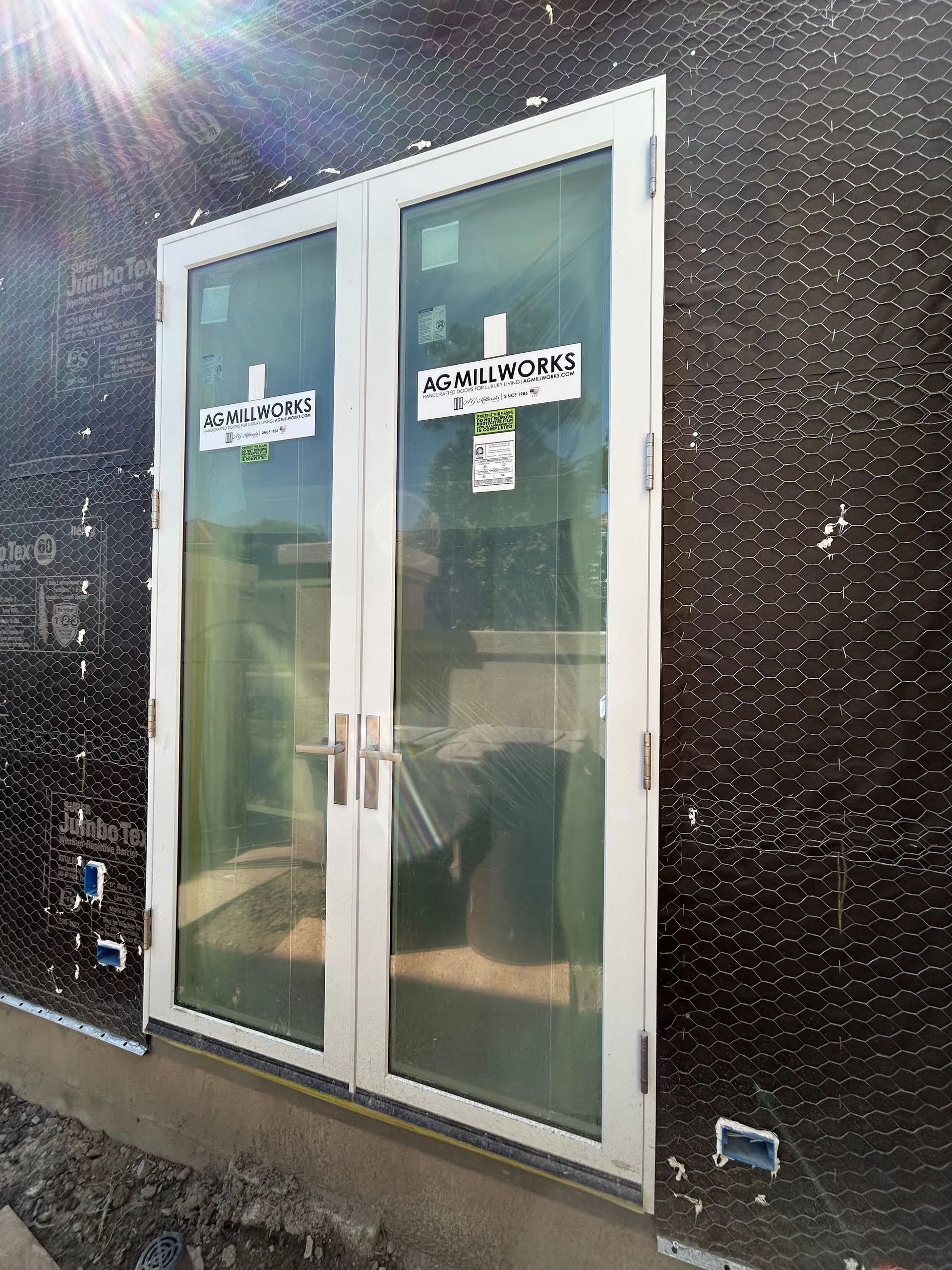 Two white-framed glass doors installed in a building's exterior wall. Black texture siding surrounds the doors.