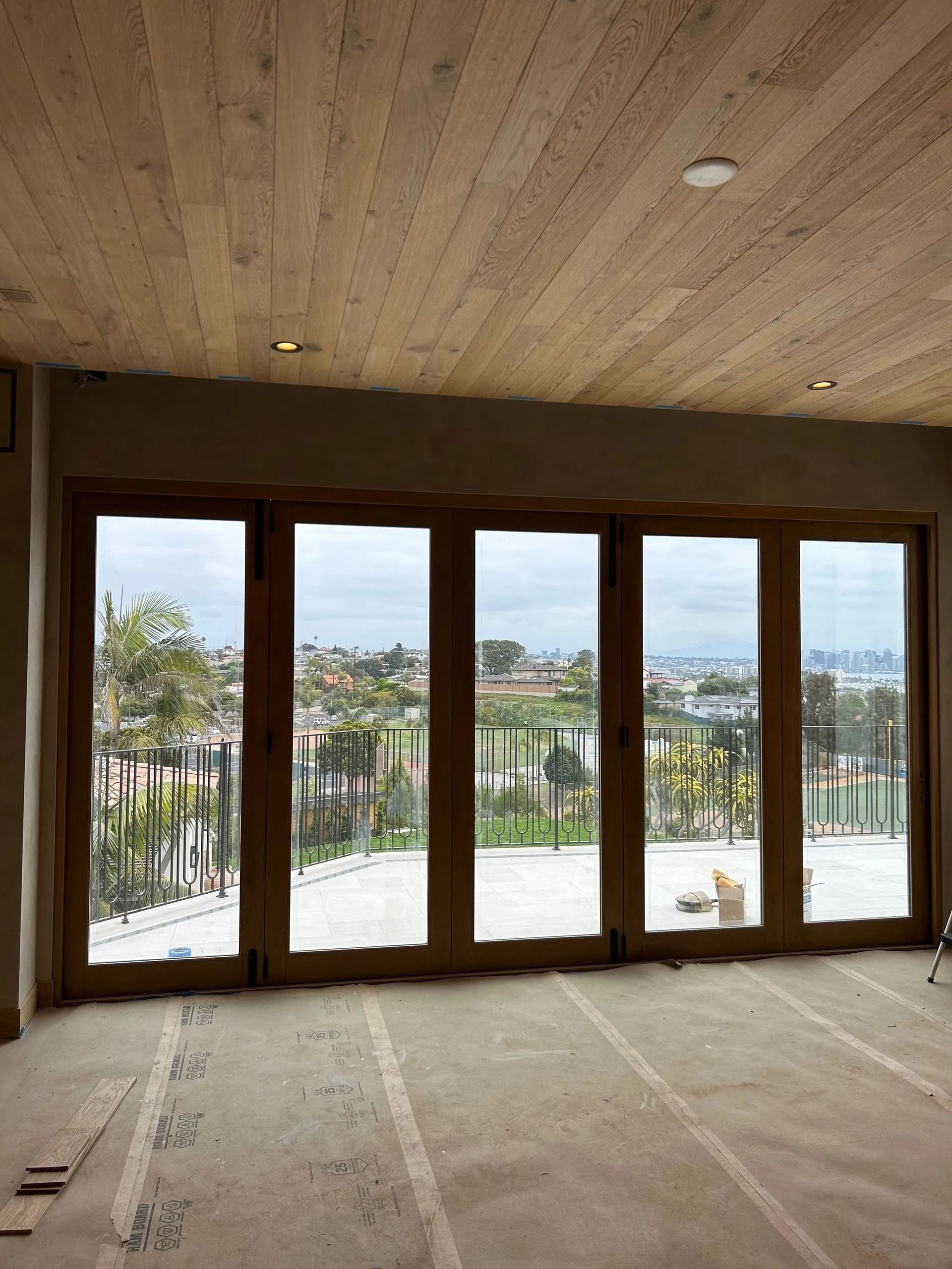 Large wooden-framed glass doors open to a cityscape view, beige walls and ceiling, unfinished interior.