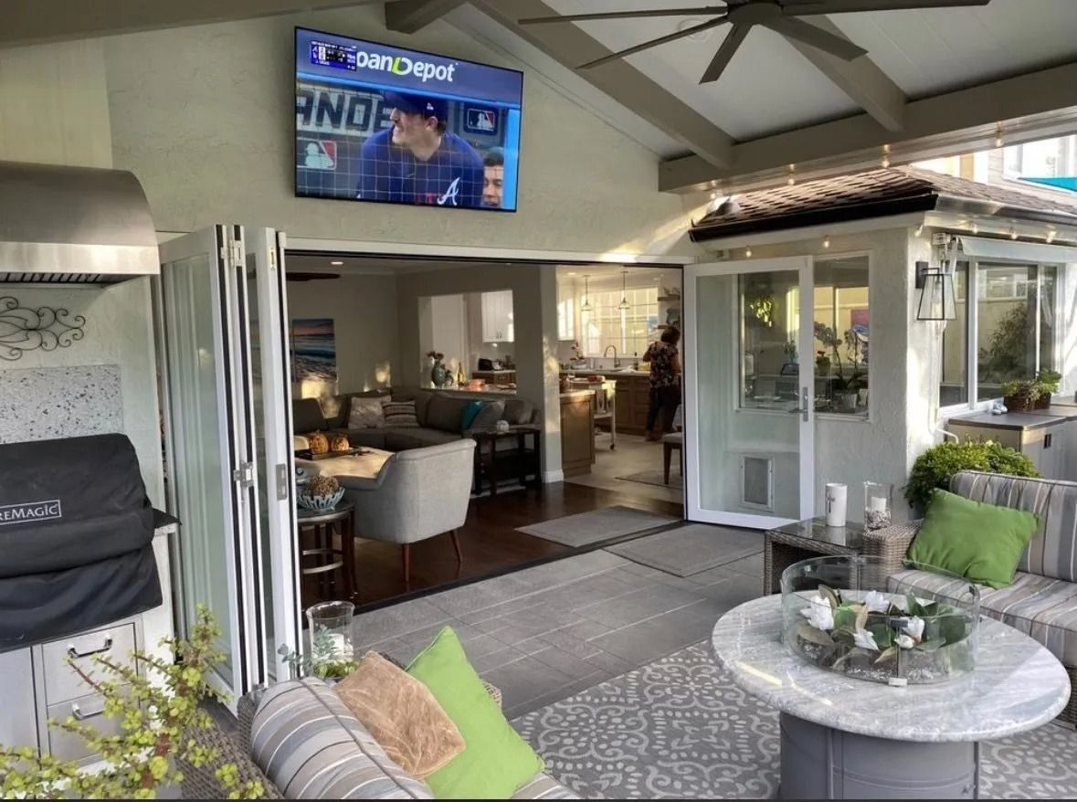 Outdoor patio with folding glass doors, TV, grill, and seating area.