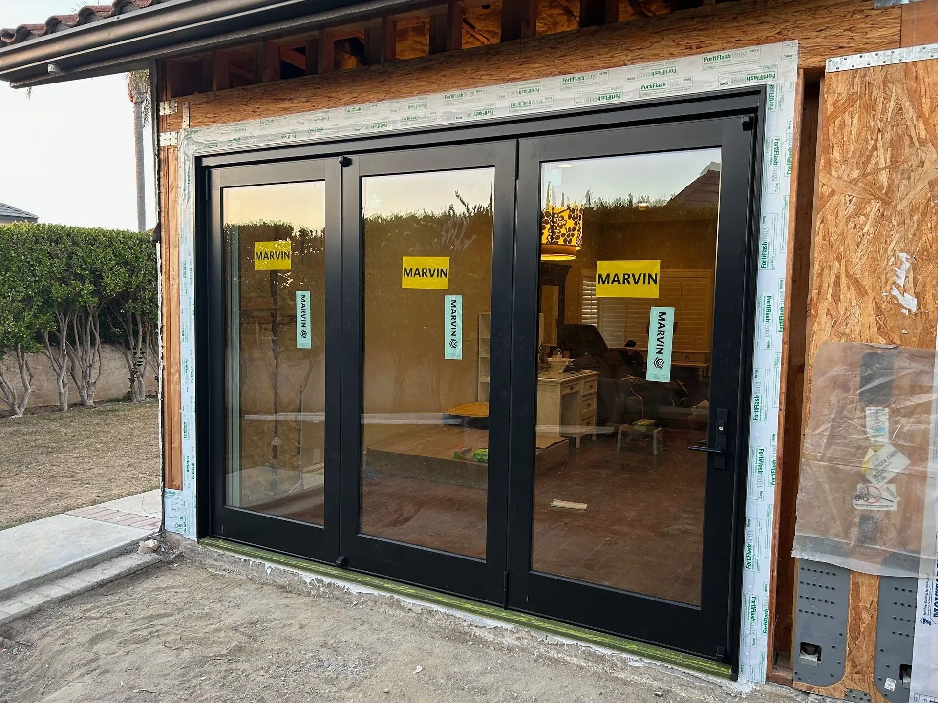 Exterior view of a newly installed, black-framed, folding glass door set in a building under construction.