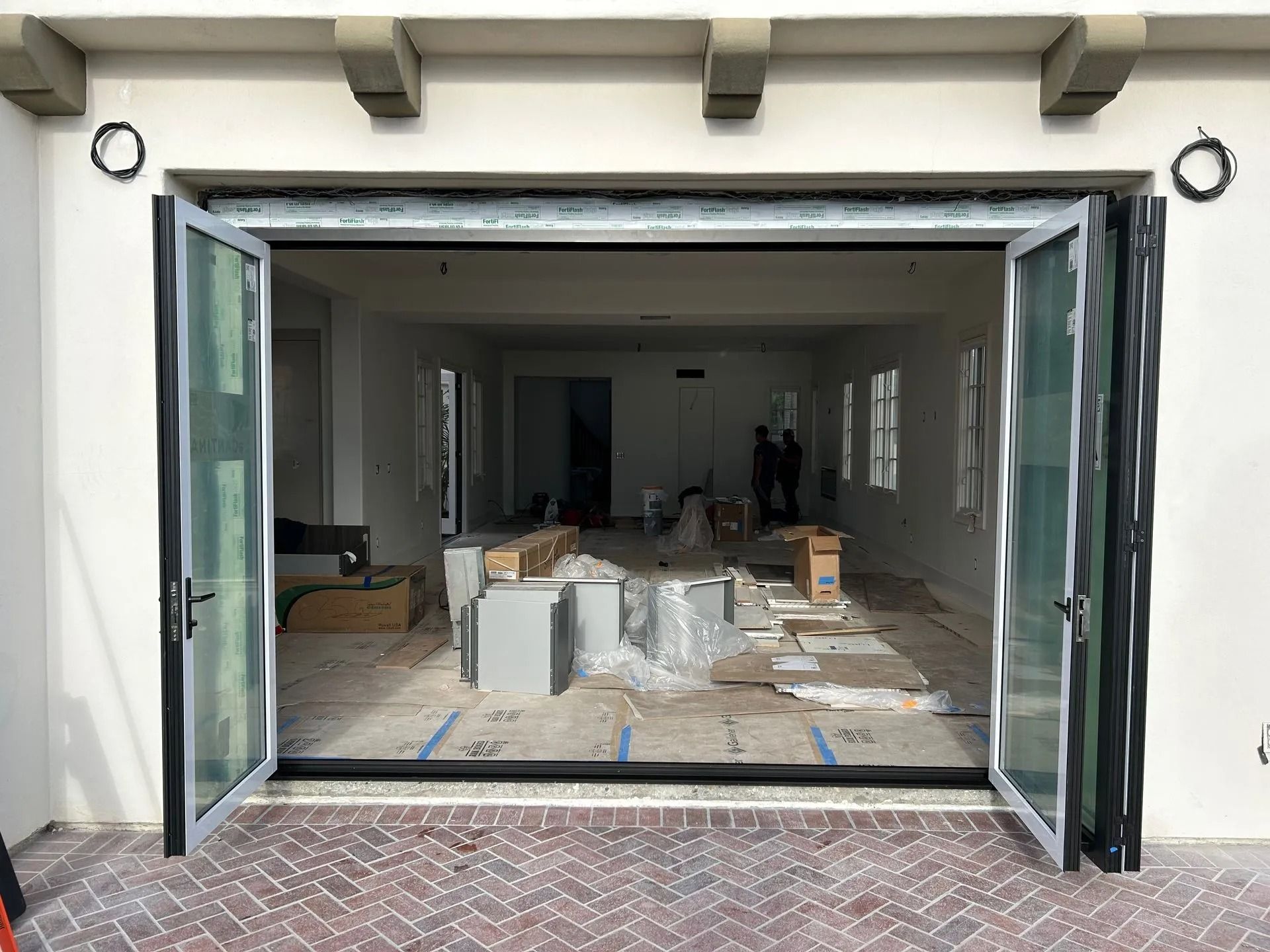 Open glass folding doors lead into a room under construction; brick patio.