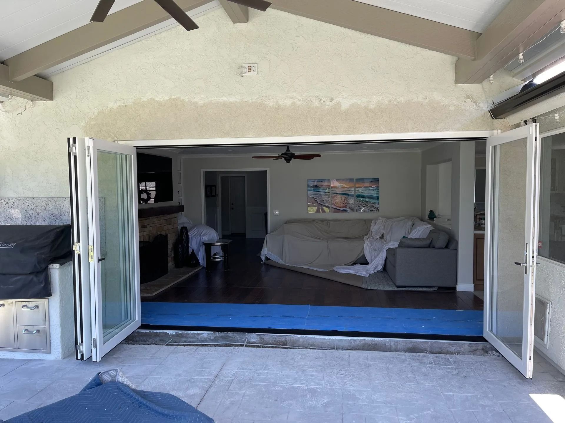 Open folding doors leading into a living room with a covered sofa, and fireplace. Exterior patio area.