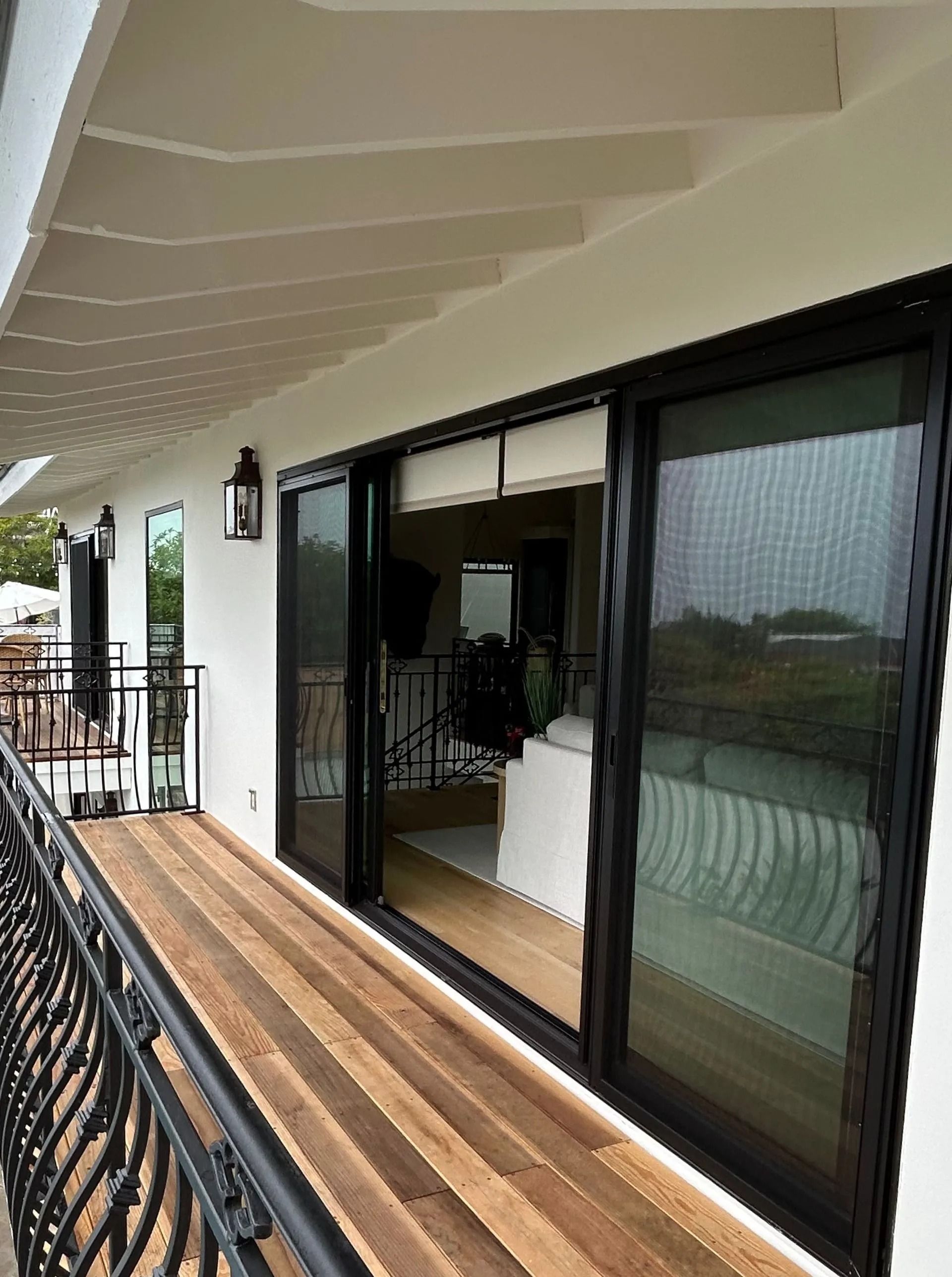 Balcony with wood flooring, black railing, and sliding glass doors leading to a room.
