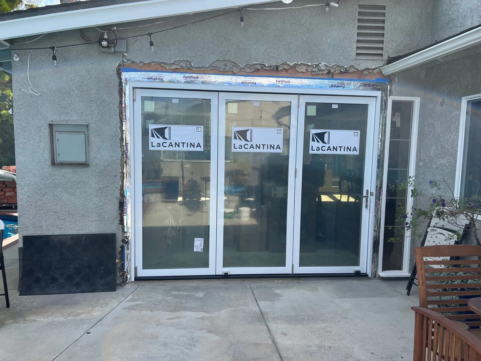 Exterior view of a house with a newly installed white folding door. Building materials and window coverings are visible.