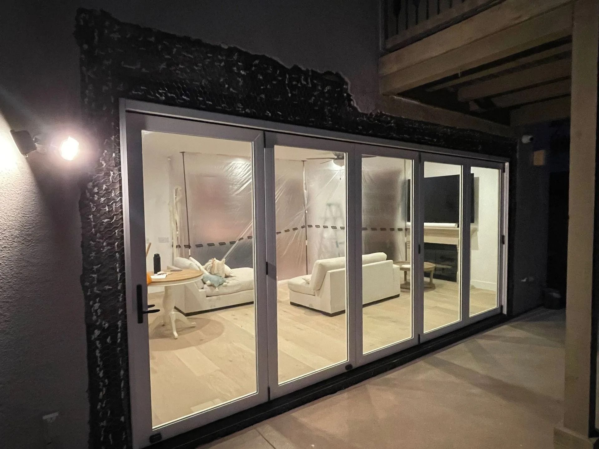 Large glass doors open to a living room with white sofas. The doors are framed by dark trim.
