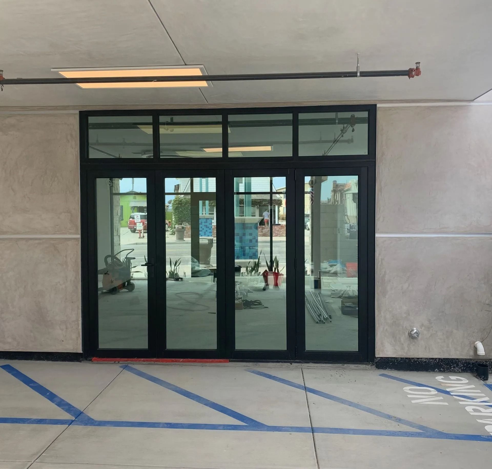 Glass doors with black frames in a building entrance, set in concrete, with blue parking lines.