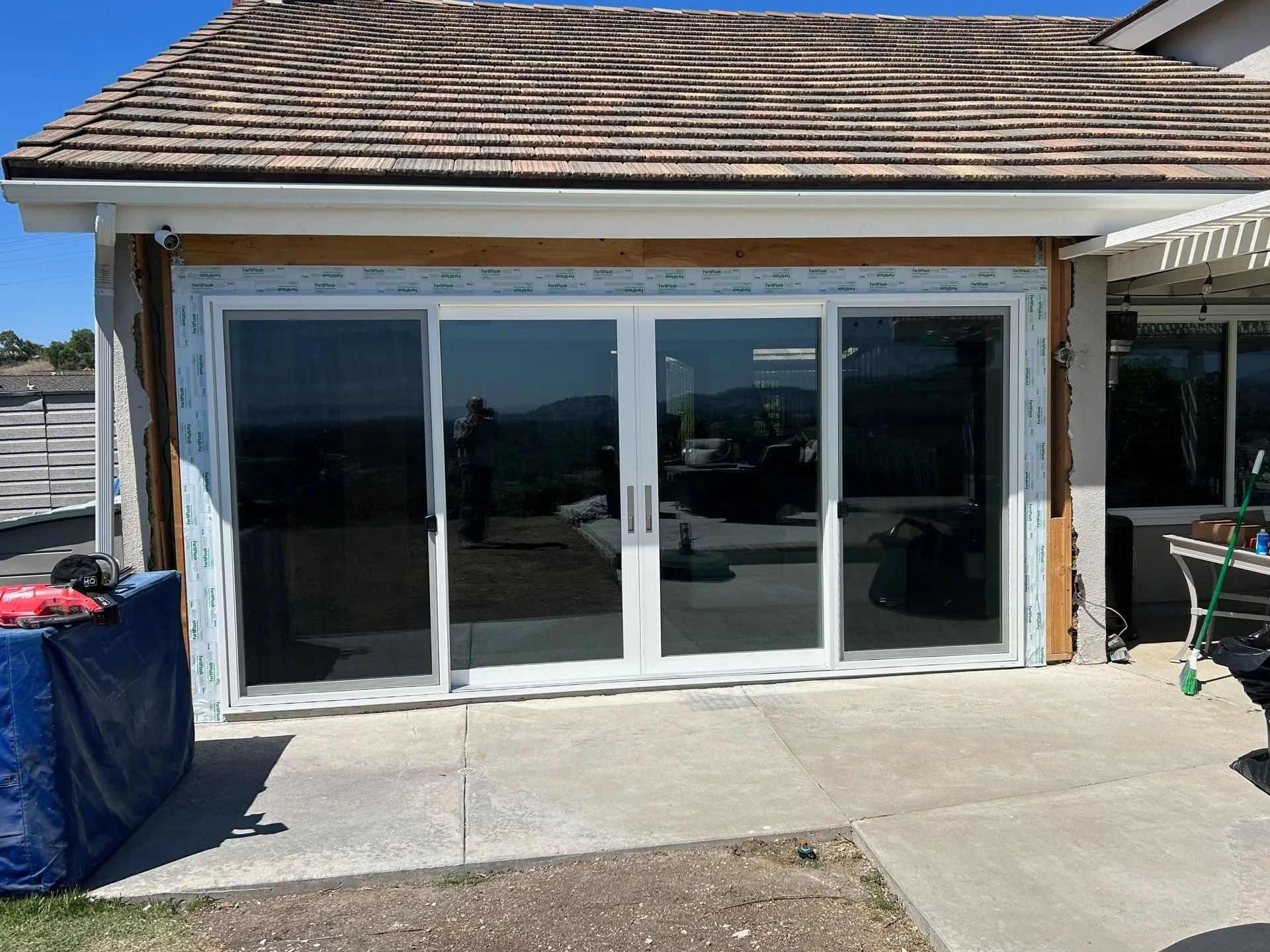 Sliding glass doors installed on a home's exterior, with surrounding wood framing and a view of hills.