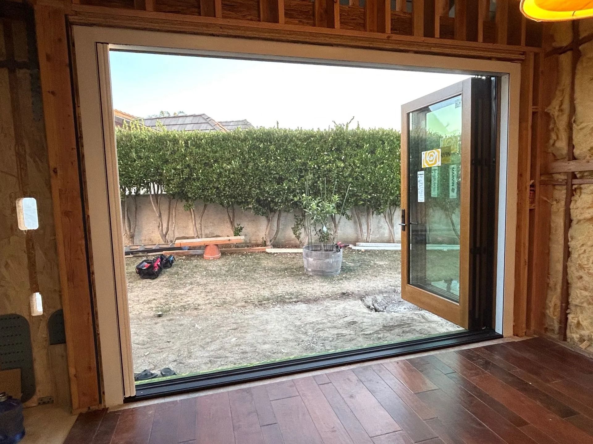Open doorway to a backyard; wooden floor, view of green hedge, clear sky, and some yard equipment.