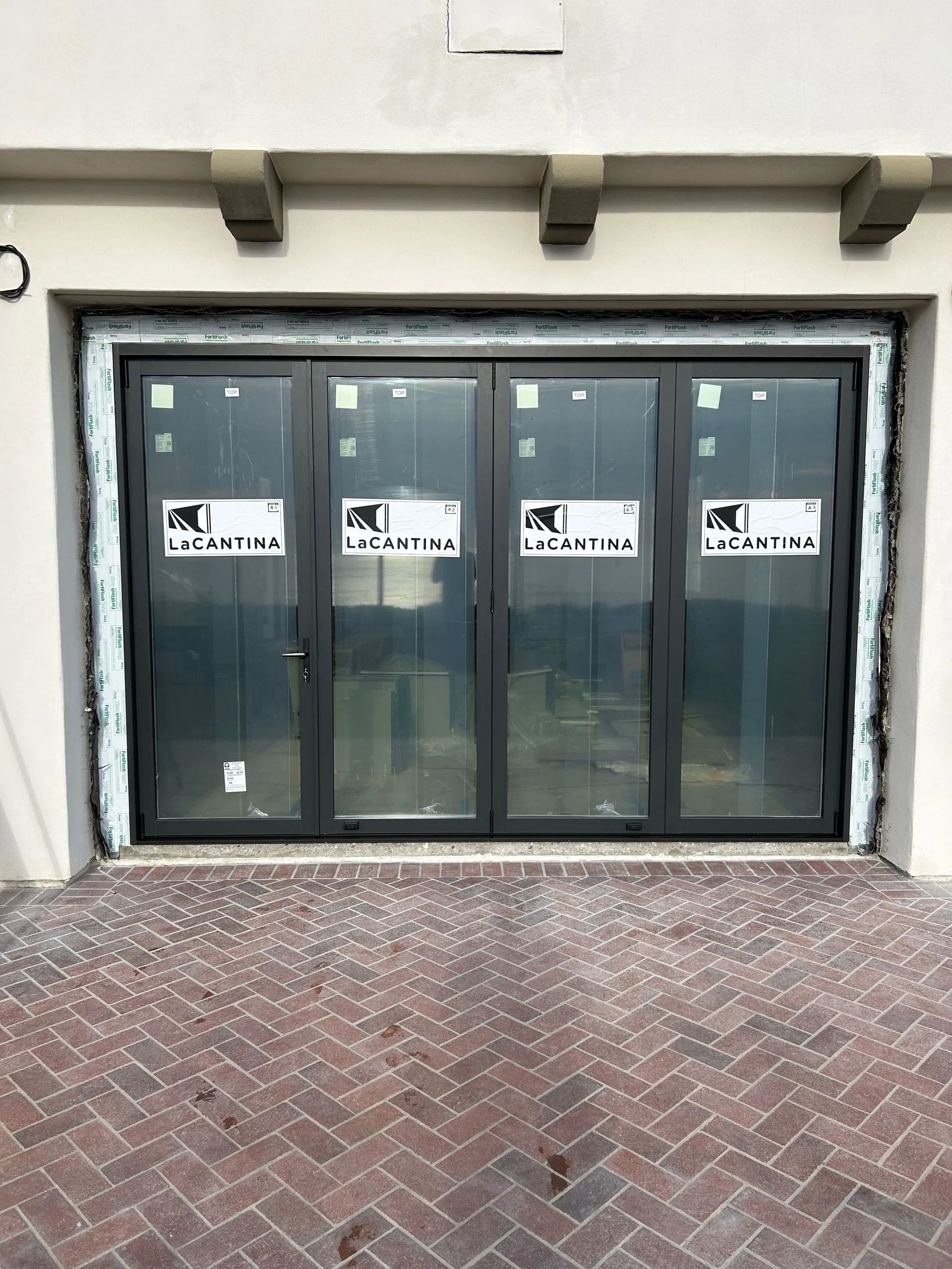 Four-panel glass door, dark frame, installed in a brick-lined entrance.