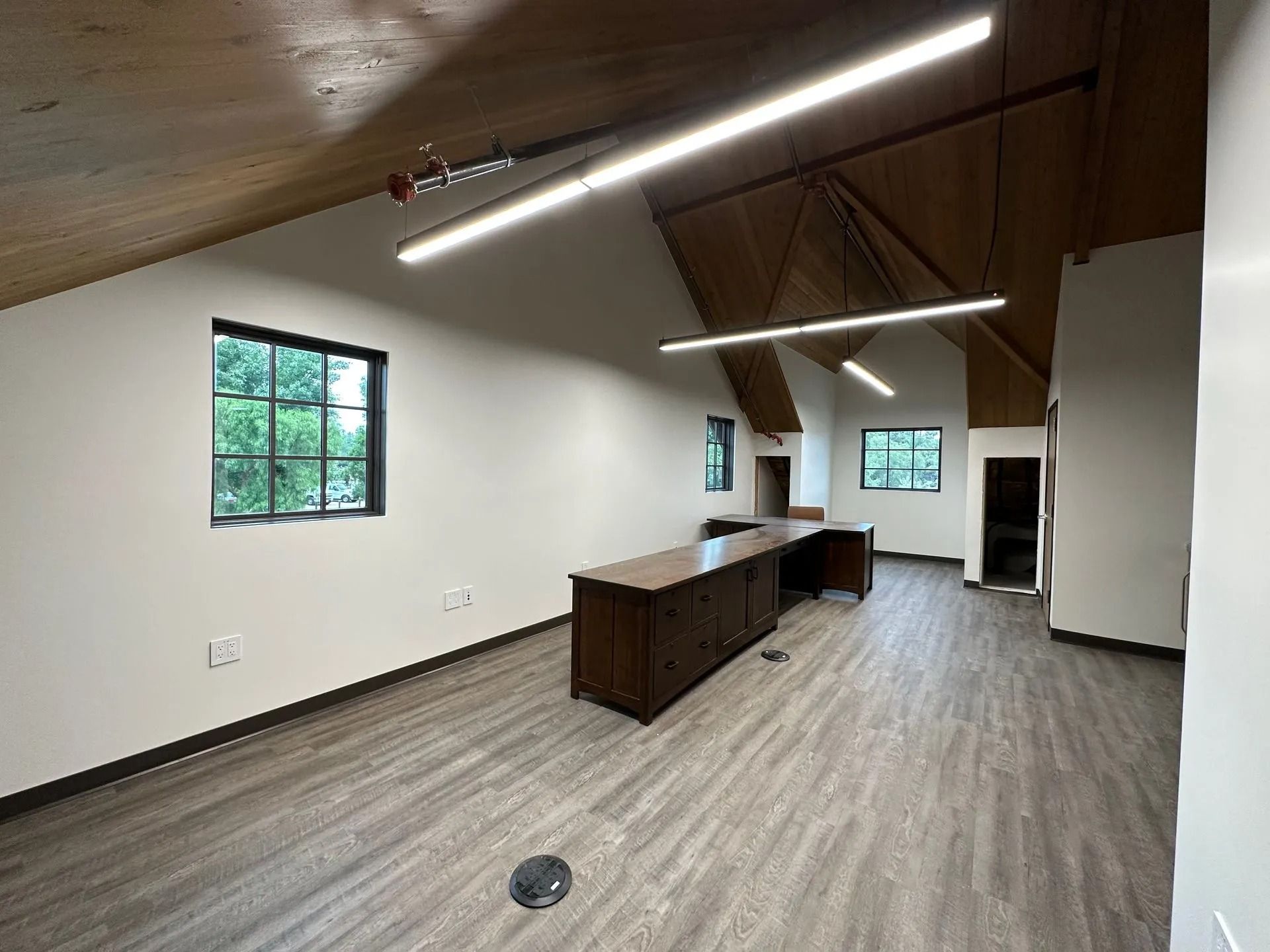 Empty office space with high ceiling, wood beams, and large desk. Gray flooring and white walls.