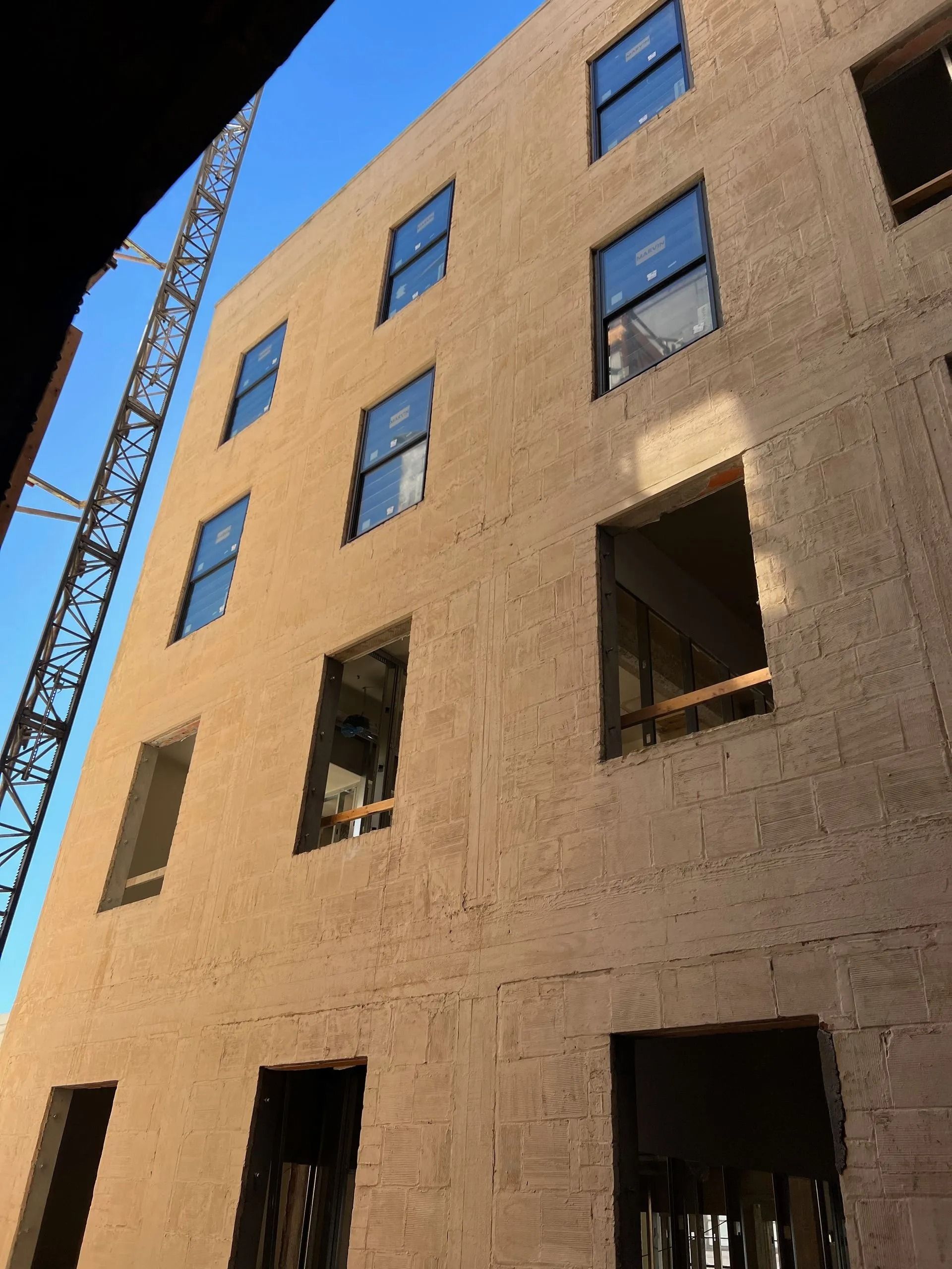 Building under construction with square window frames. Light brown exterior with crane in view against a blue sky.