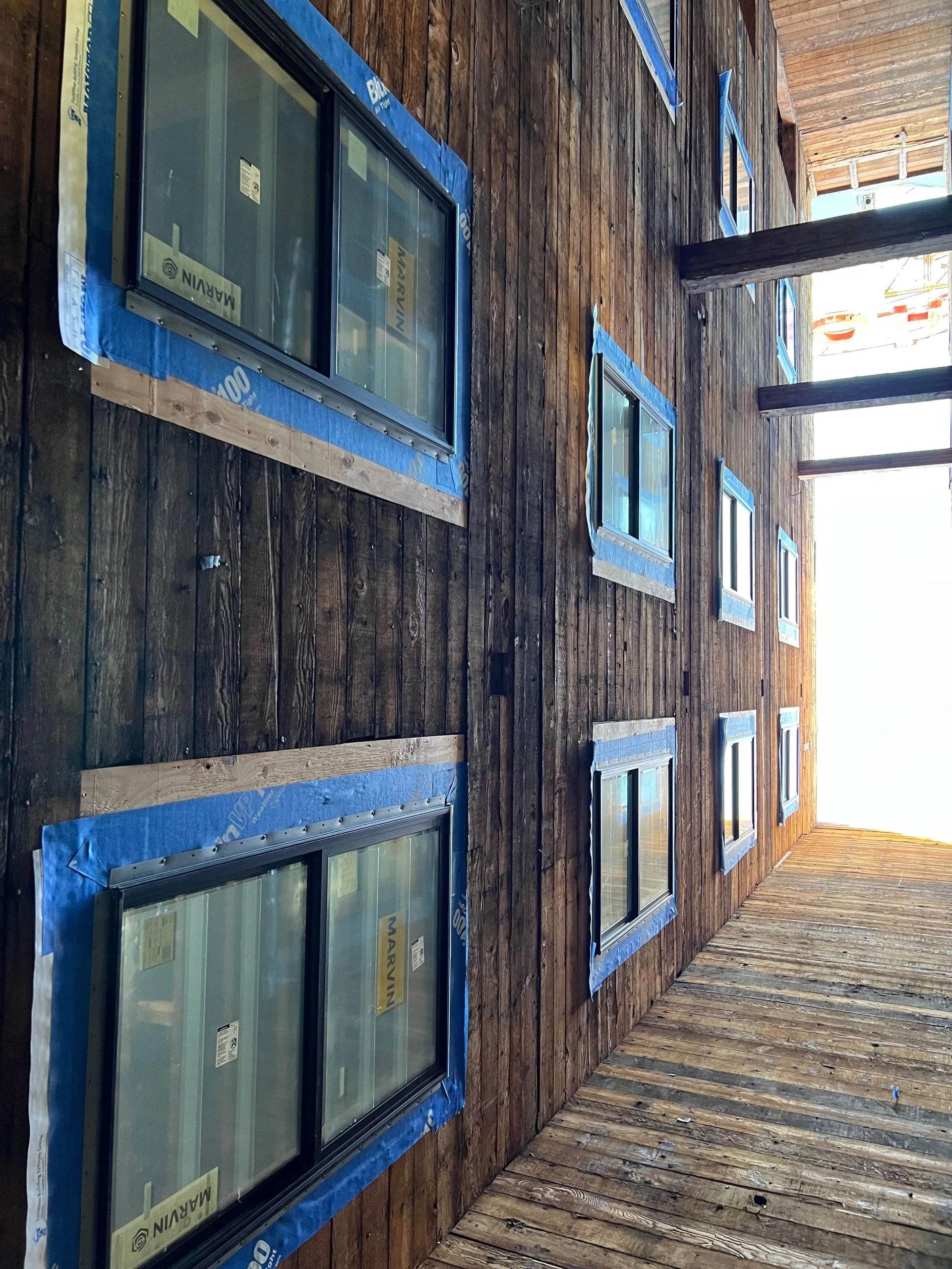 Weathered wood wall with rectangular windows, blue trim. Sunlight streams from the end.
