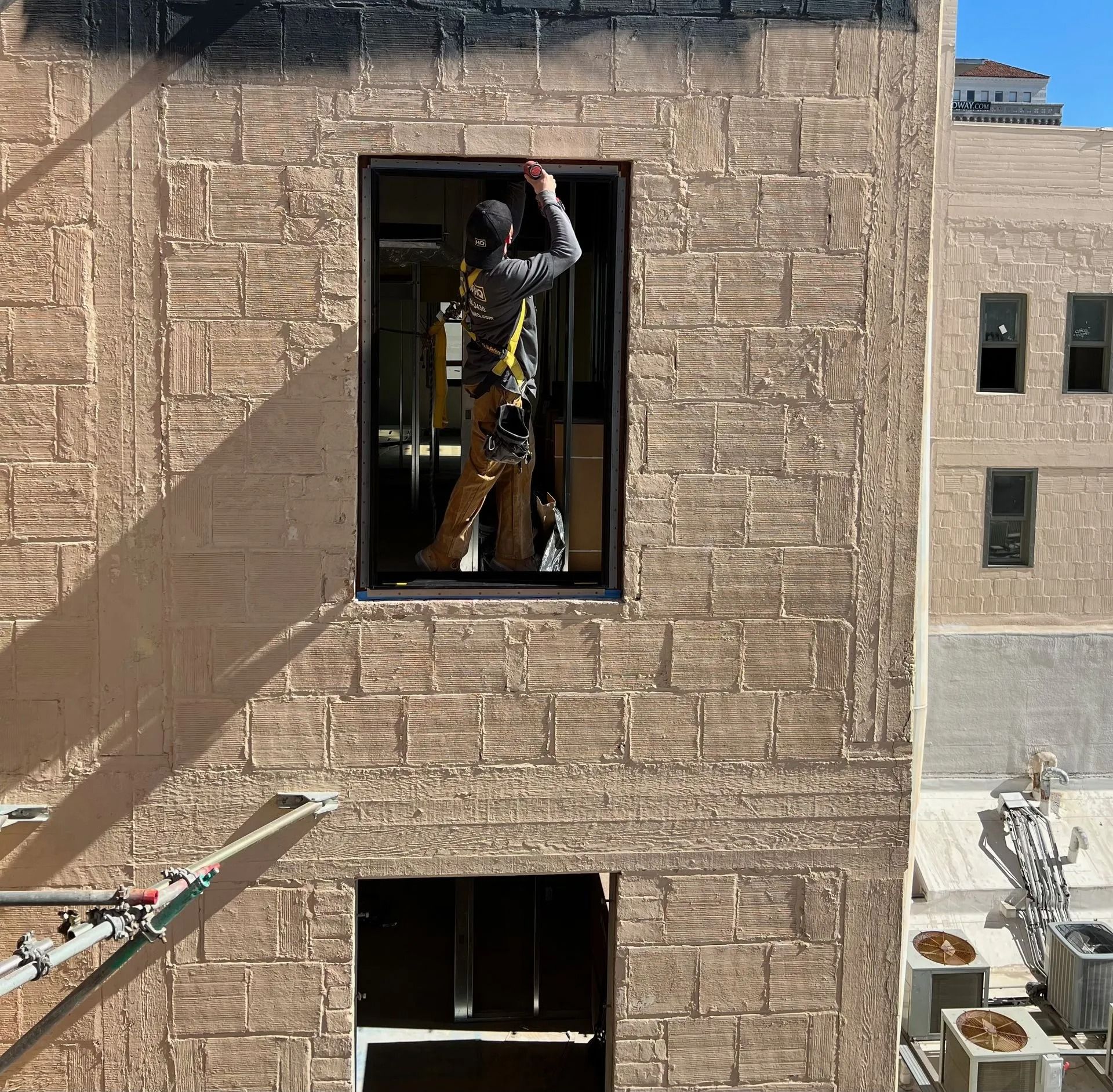 Construction worker in a window opening, on an exterior wall with textured surface. Scaffolding visible below.