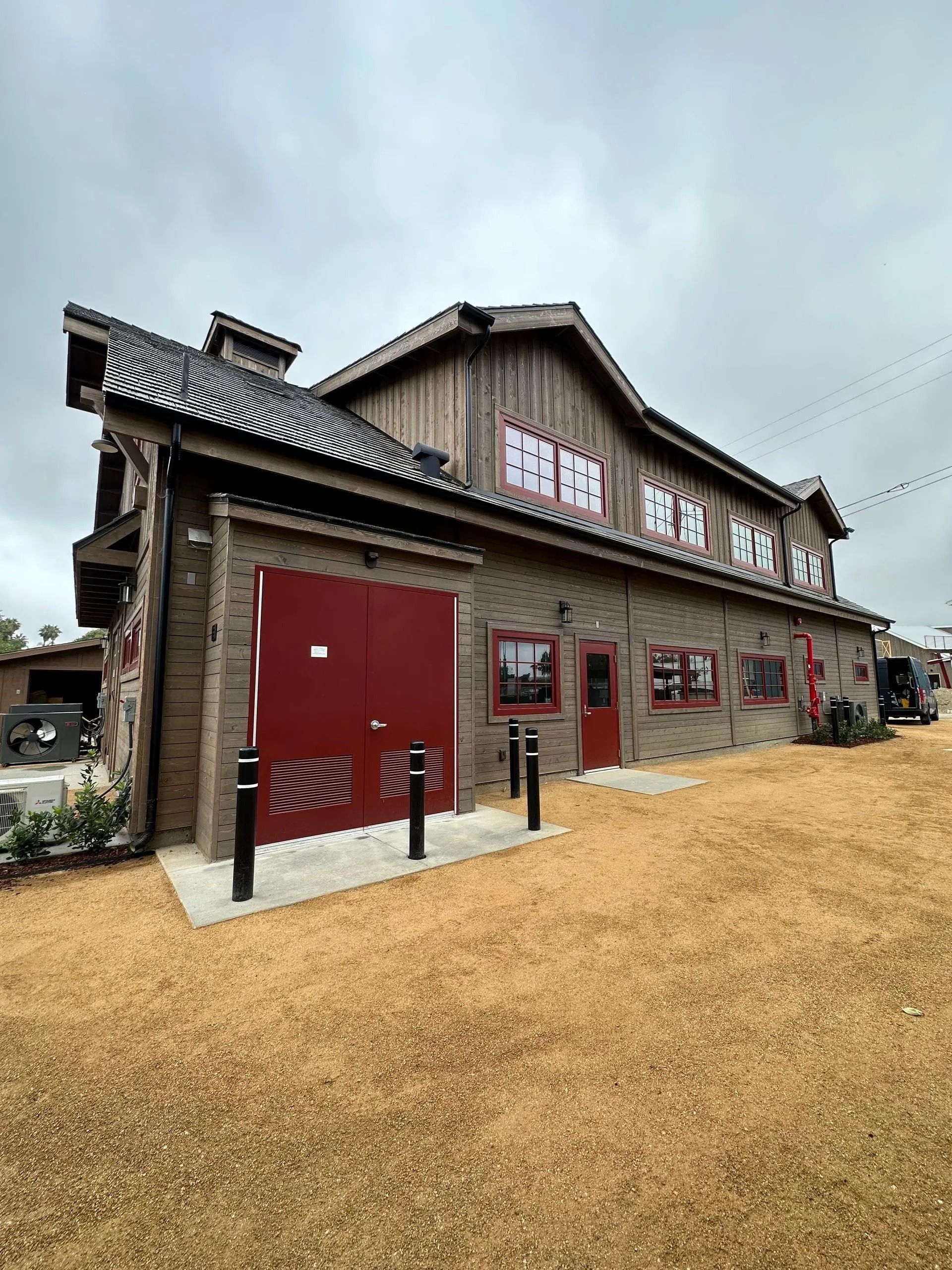 Brick and wood building with red doors and windows. Exterior shot on a gravel lot under an overcast sky.