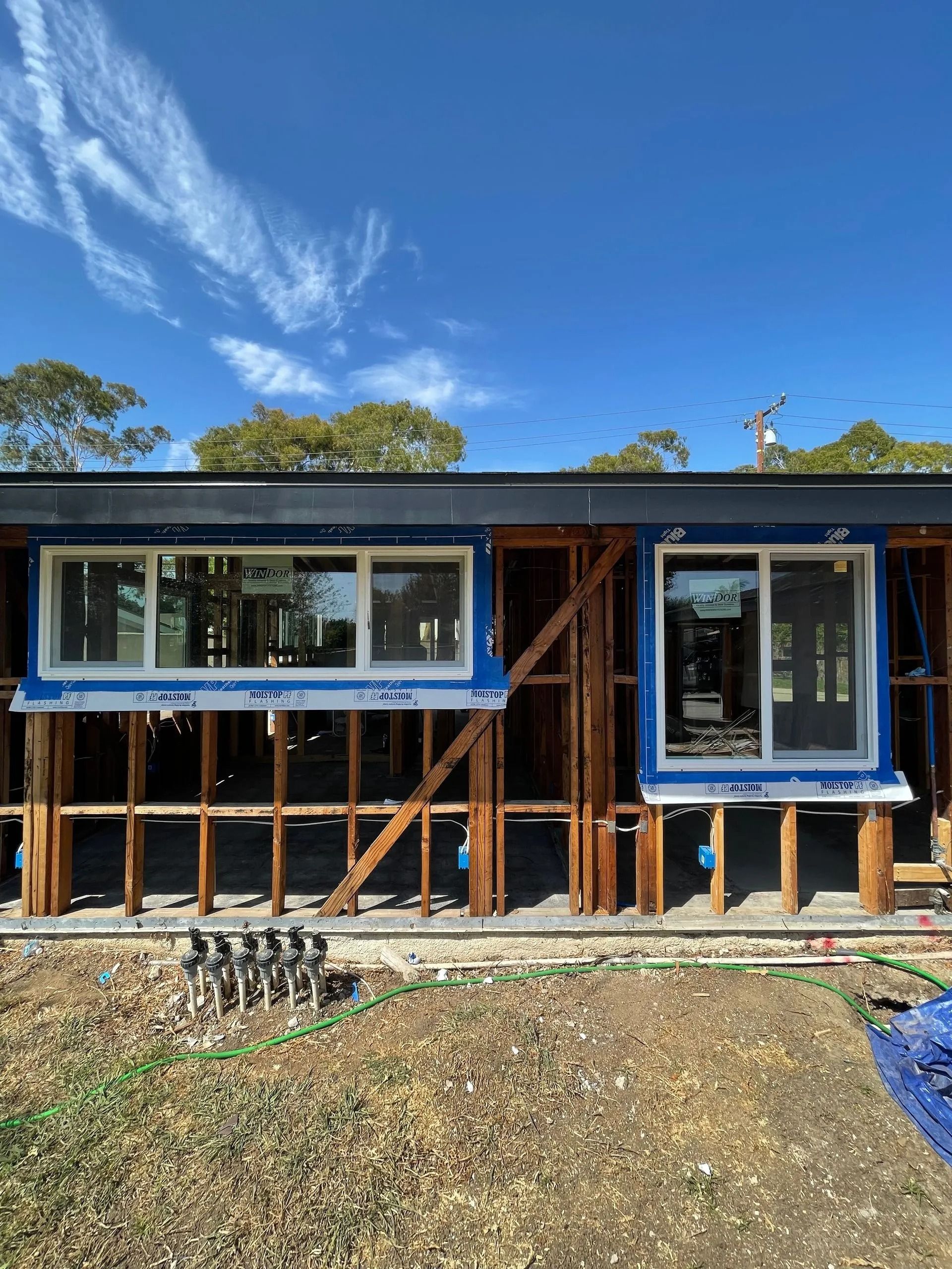 Exterior of building under construction; wooden frame with installed windows, blue sky overhead.