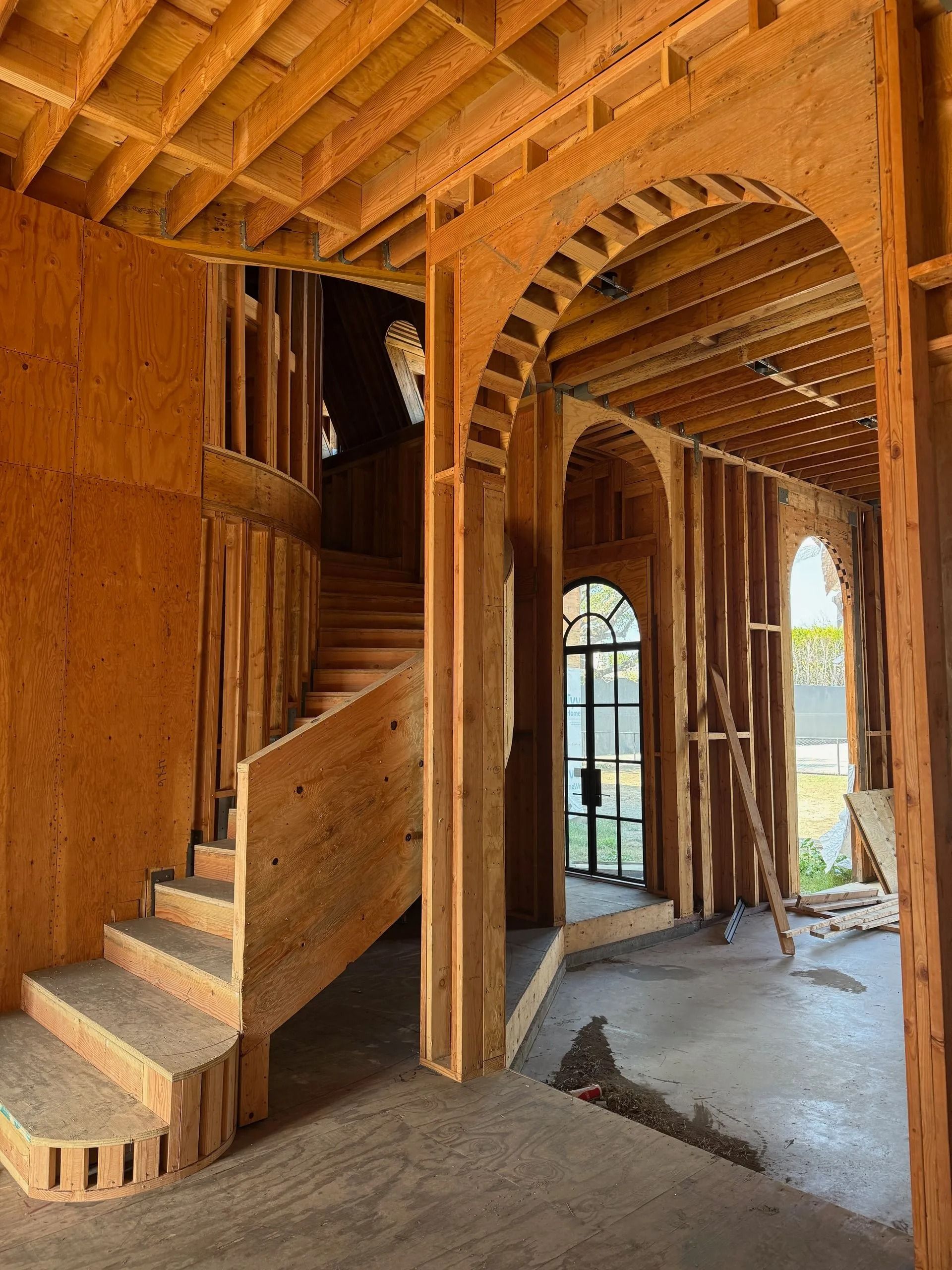 Wooden interior under construction: arched doorways, staircase, exposed framework.